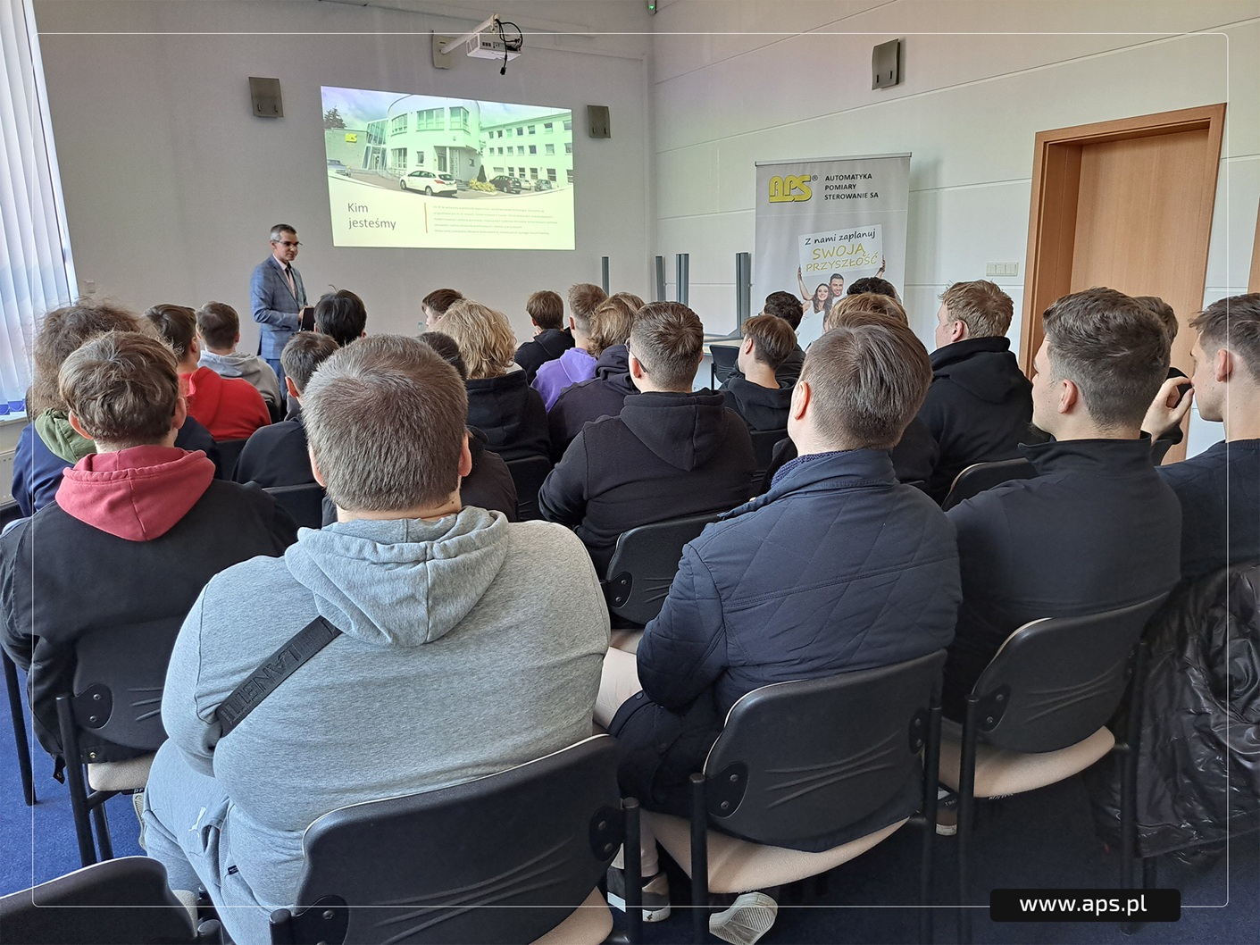 Studenci w sali konferencyjnej APS słuchają prezentacji na temat firmy