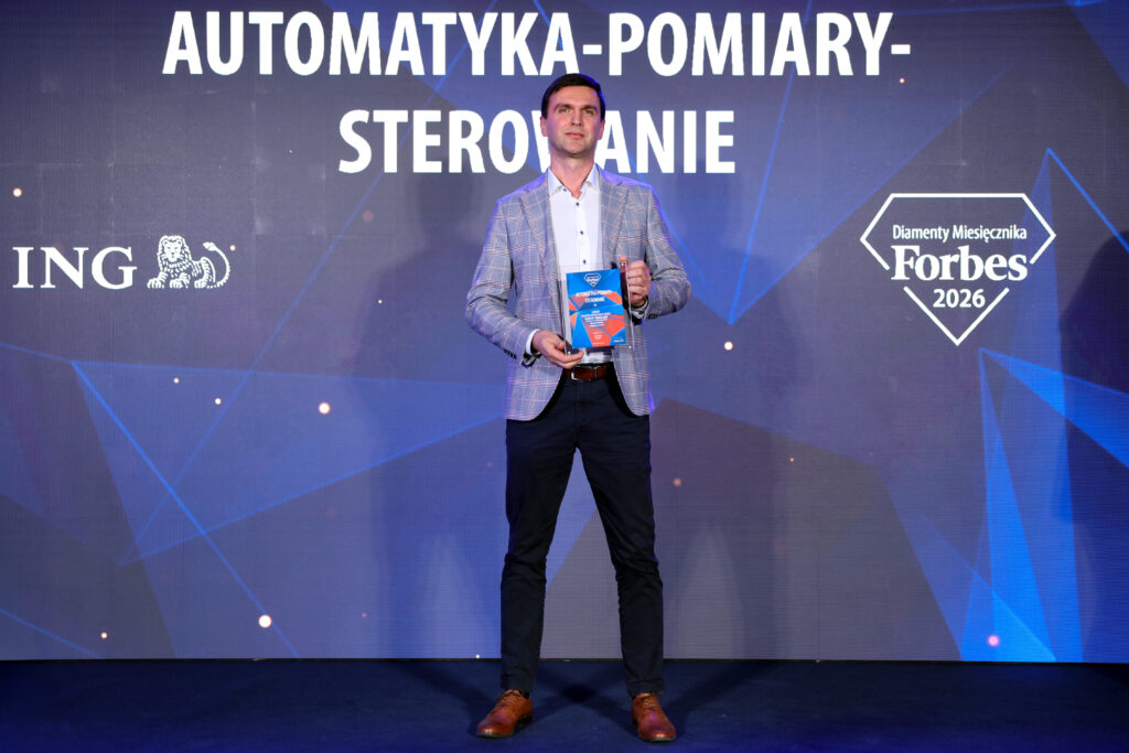 Prezes APS stoi na scenie Diamentów Forbesa, w rękach przed sobą trzyma certyfikat laureata rankingu
